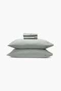 Set of light green bedding including a folded sheet, two pillows, and a sheet on a white background.