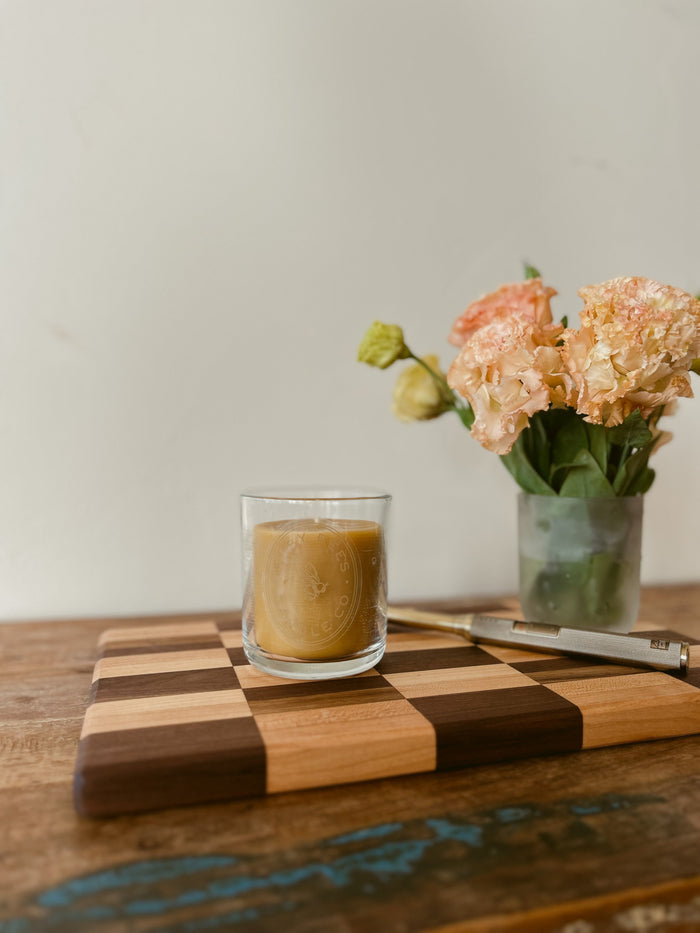 Busy Bees Classic Beeswax Jar Candle 12oz styled beside flowers and stacked books on a cozy wooden table.