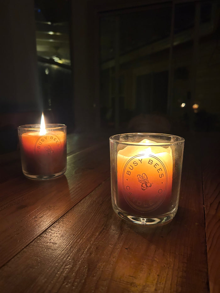 Busy Bees Classic Beeswax Jar Candle 12oz glowing on a wooden table in a dimly lit evening setting.
