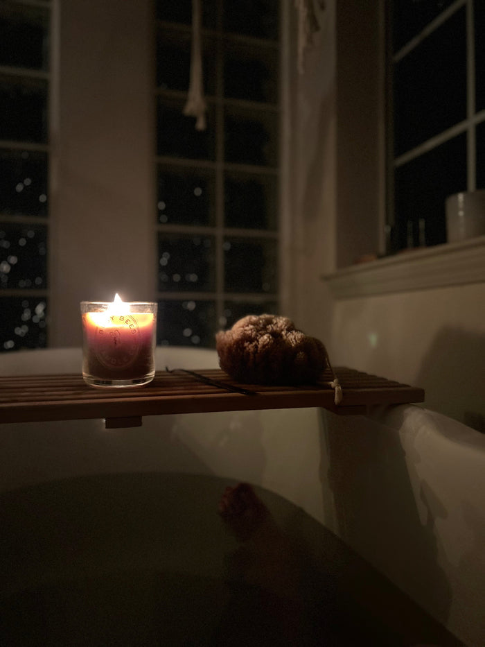Lit Busy Bees Classic Beeswax Jar Candle 12oz displayed on a countertop beside a window in a softly lit room.
