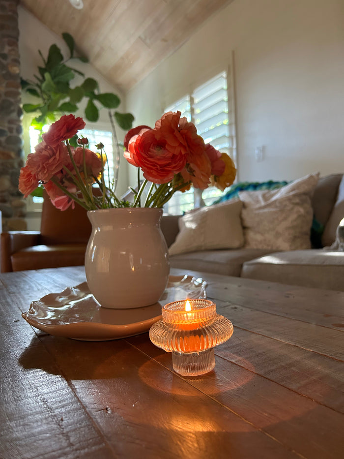 Busy Bees Glass Lantern set of 2 styled on a wooden table beside flowers and a lit tea light candle in a cozy living room setting.