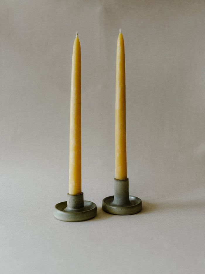 Two lit Busy Bees Hand Dipped 9 Inch Taper Candles displayed in brass holders against a neutral background.