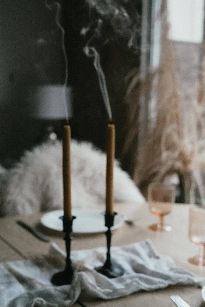 Lit Busy Bees Hand Dipped 9 Inch Taper Candles displayed beside glassware in a moody indoor setting.