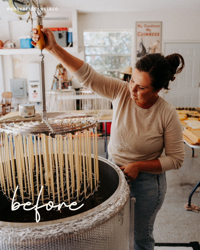 Person arranging multiple lit Busy Bees Hand Dipped 9 Inch Taper Candles on a dining table in a softly lit room.