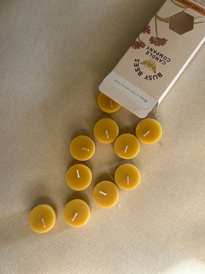 Busy Bees Tea Light Candles Box 10ct with loose natural beeswax tea lights spilling from branded packaging onto a soft neutral surface.