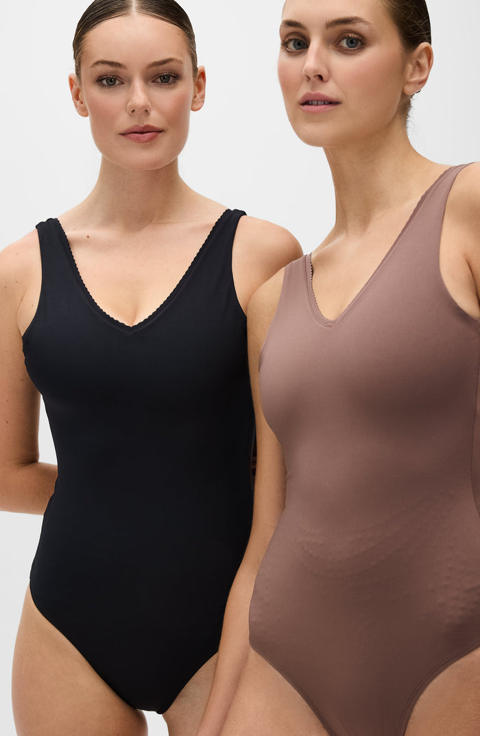 Two women standing side by side wearing the Elastique Athletics Adorn bodysuit in black and taupe colorways against a neutral background.