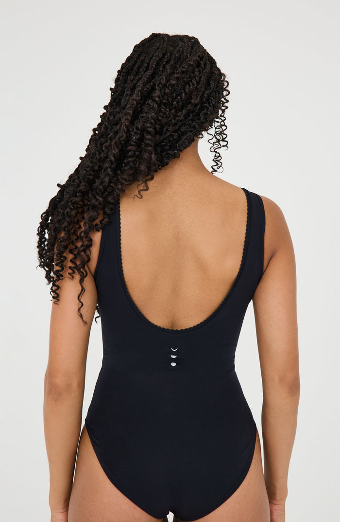 Back view of a woman wearing the Elastique Athletics Adorn black sleeveless bodysuit with a low scoop back design.