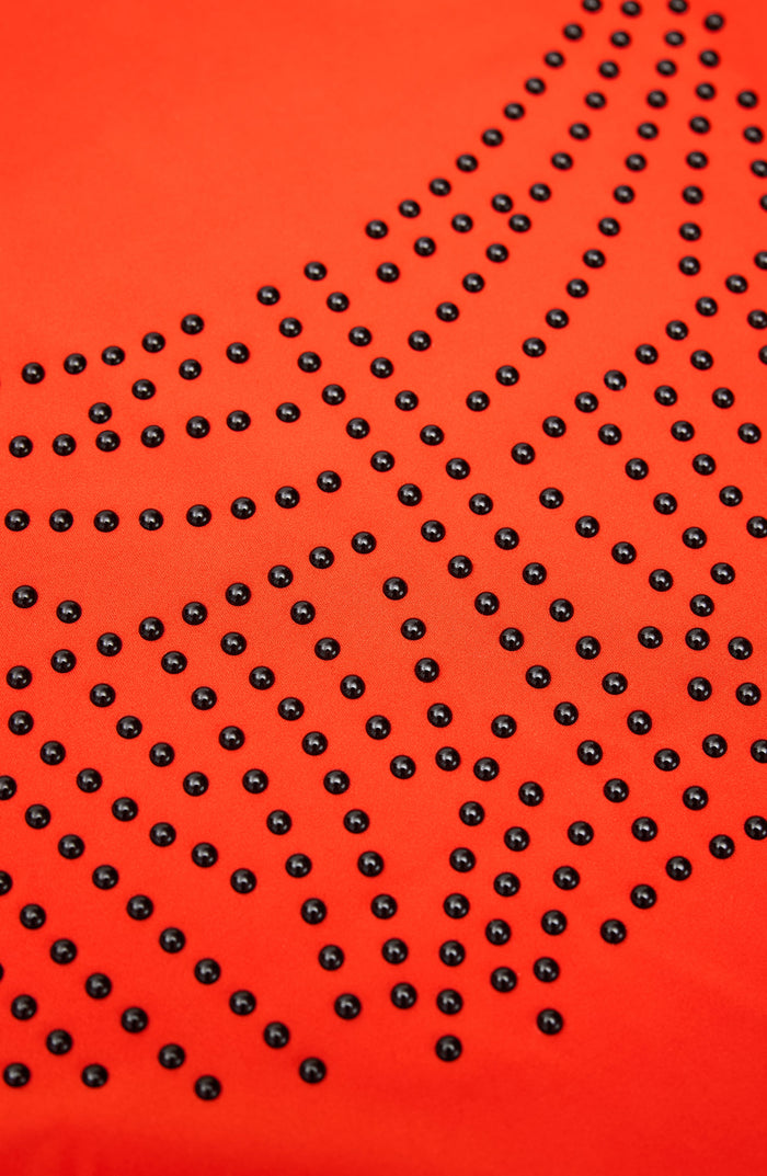 Abstract close up pattern detail associated with the Elastique Athletics Adorn collection featuring black dotted lines on a bright orange background.