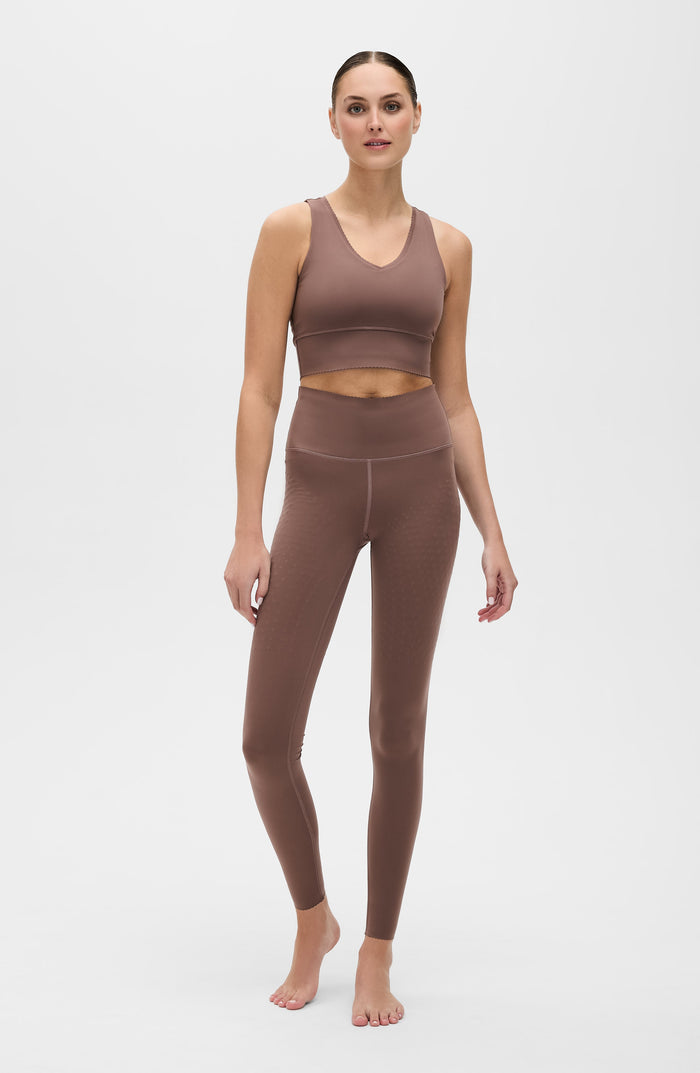 Full body portrait of a woman wearing the Elastique Athletics Adorn Leggings in taupe with a matching sports bra against a neutral background.