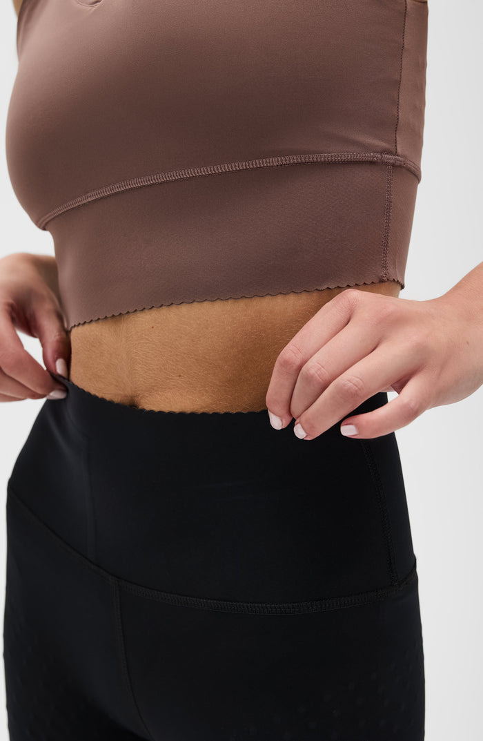 Close up waistband detail of the Elastique Athletics Adorn Leggings in black paired with a taupe sports bra.