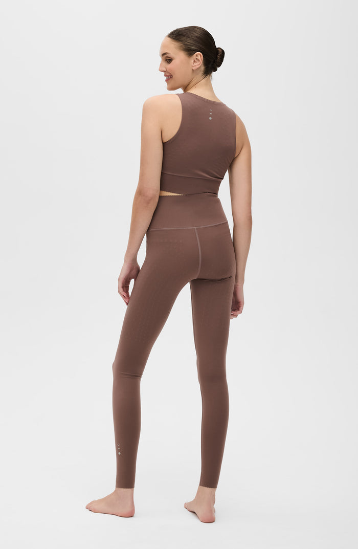Back view of a woman wearing the Elastique Athletics Adorn Leggings in taupe with a matching sports bra.