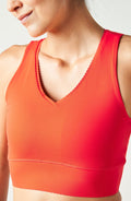 Close-up of a person wearing an Elastique Athletics Adorn orange sports bra against a light background