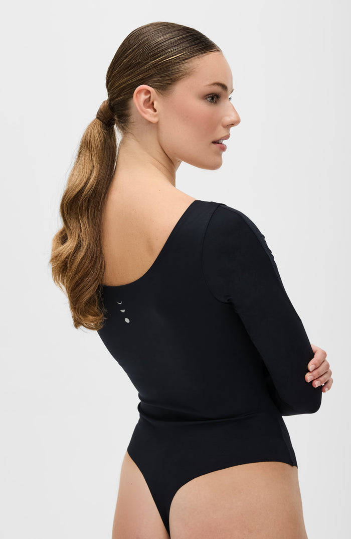 Back view of a woman wearing the Elastique Athletics Iconic Compression Long Sleeve Bodysuit Thong in black with long sleeves and a low scoop back.