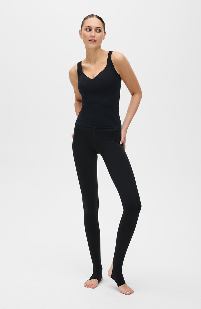 Full body studio portrait of a woman posing in the Elastique Athletics Iconic MicroPerle Tank in black with matching leggings.