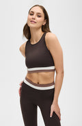 Woman smiling while wearing the Elastique Athletics Le Monde Bra in dark brown with white trim and matching high waisted leggings.