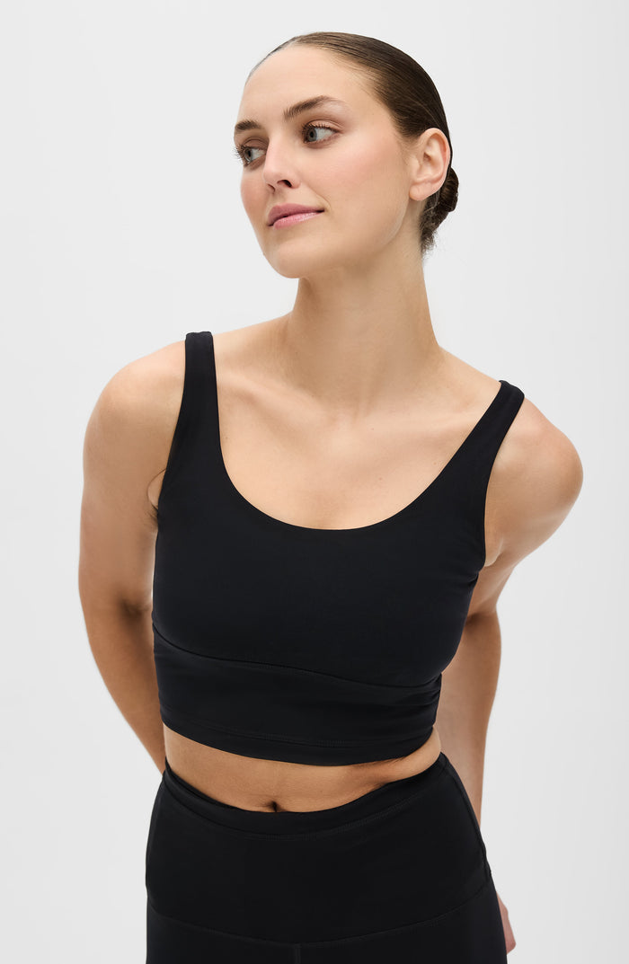 Woman posing with her hands behind her back while wearing the Elastique Athletics Lisse Compression Bra in black with matching leggings.