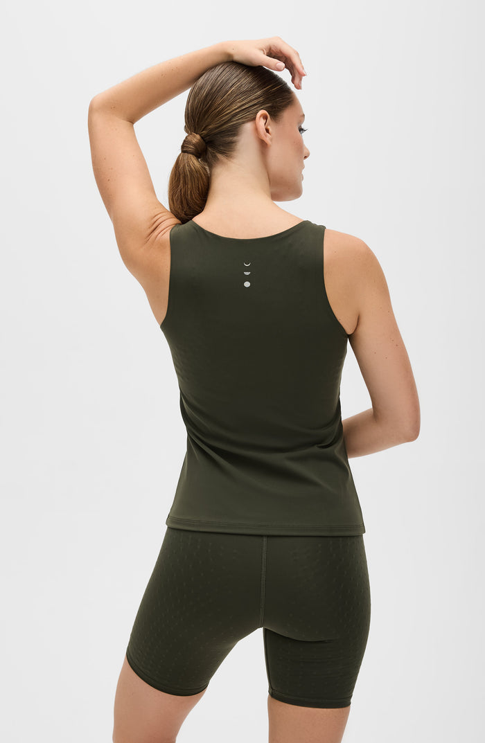 Woman posing with one arm raised while wearing the Elastique Athletics L'Original Lymphatic Tank in olive green with matching bike shorts.