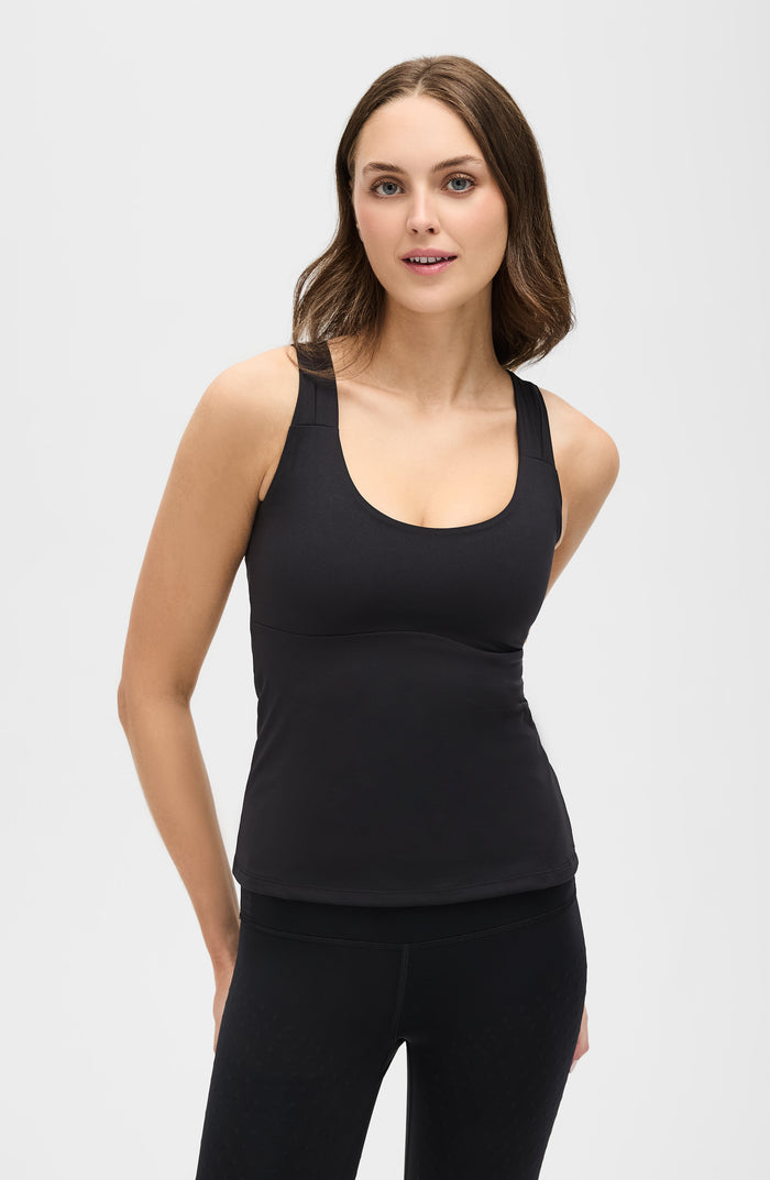 Woman standing with hands behind her back while wearing the Elastique Athletics L'Original Lymphatic Tank in black with matching leggings.