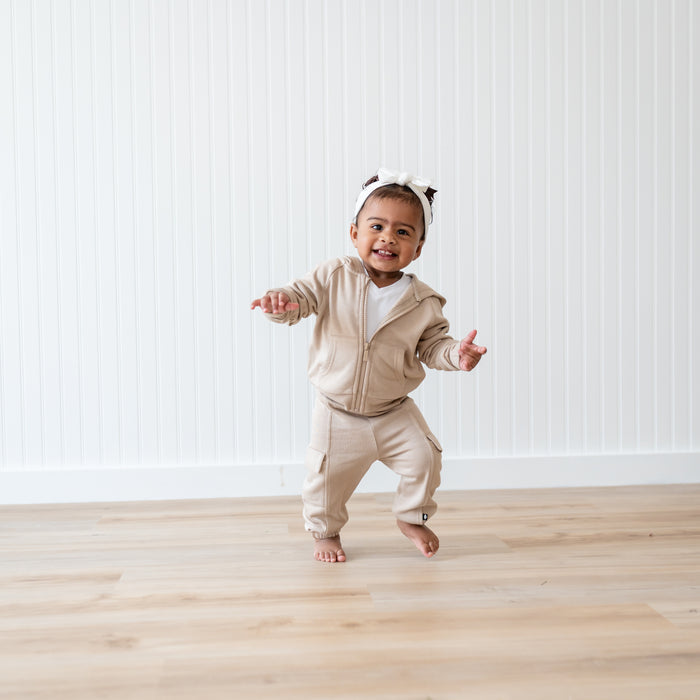 Smiling toddler walking wearing the Fleece Cargo Pants in Almond paired with an Almond Fleece Zip hoodie