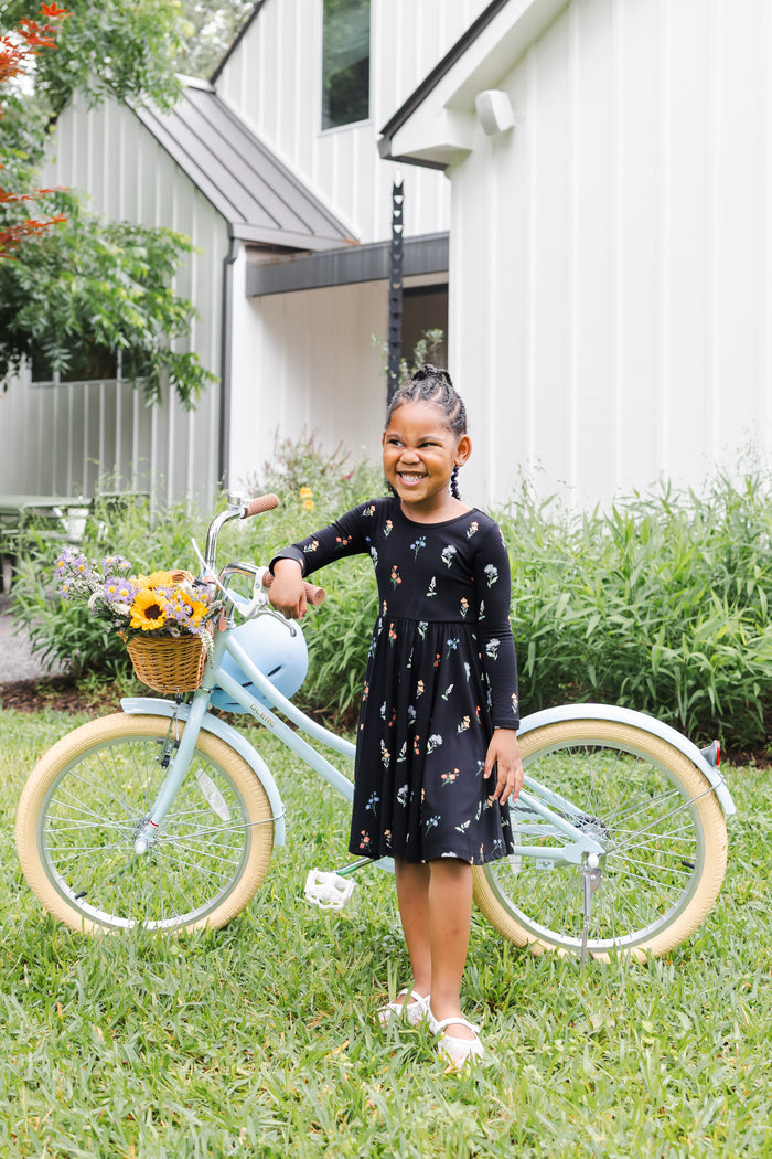 Girl standing outdoors with a bicycle in a garden wearing Long Sleeve Twirl Dress in Midnight Wildflower print