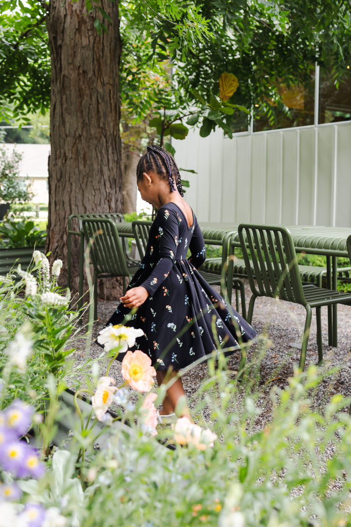 Girl playing outdoors in a garden wearing Long Sleeve Twirl Dress in Midnight Wildflower print