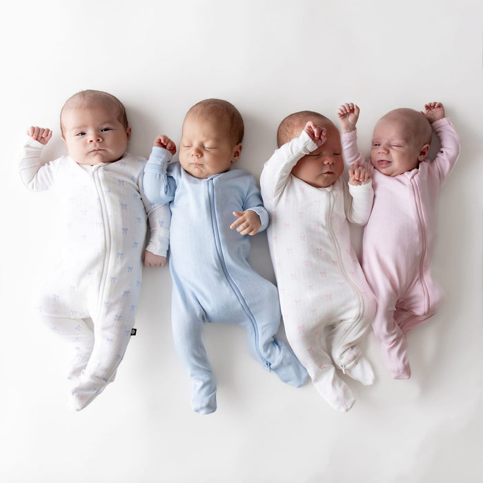 Four newborns laying side by side wearing the Pointelle Zippered Footie in Sakura, Sweet Pink Bow, Breeze and Sweet Blue Bow