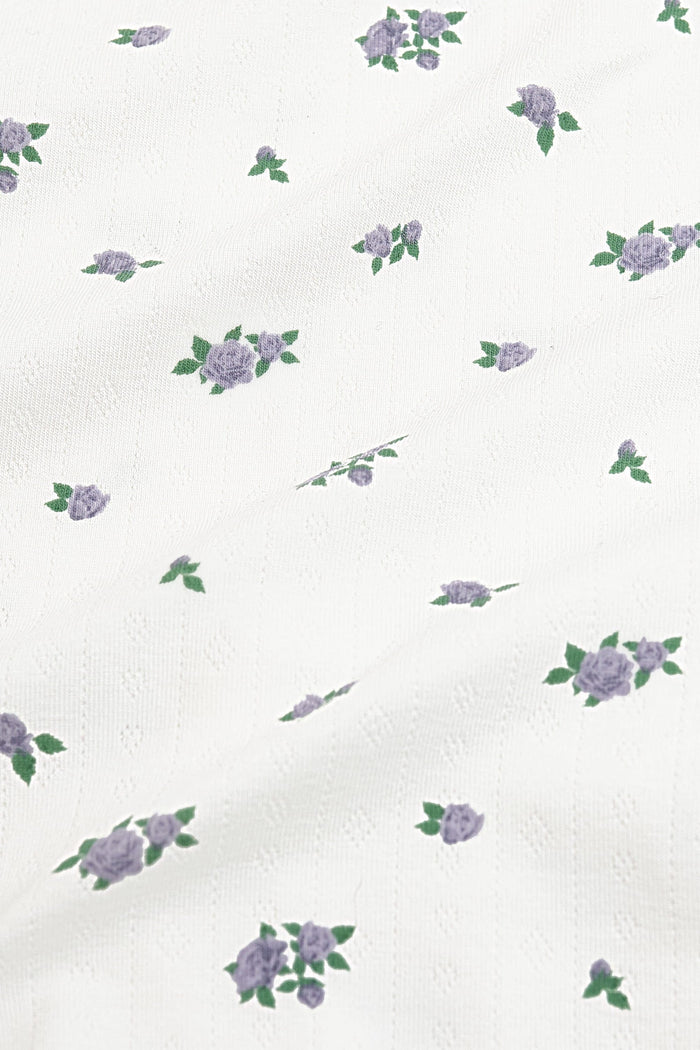 Close up of the pointelle fabric: An all-over print featuring clusters of three purple spray roses with green leaves over a white background.