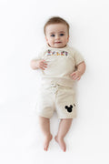 Baby wearing a cream colored matching set with mickey friends on the shirt and black mickey head on the short