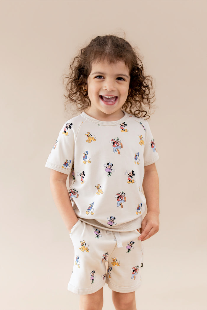Toddler wearing a cream matching tshirt and short set with mickey and friends pattern