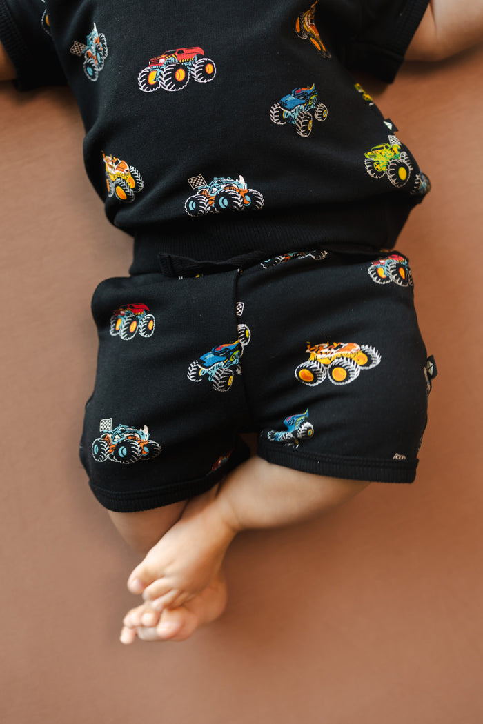 Baby wearing Black Short Joggers in Monster Truck print on beige background