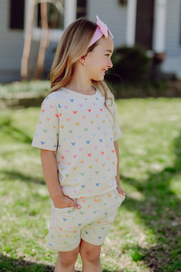 Young girl wearing a light-colored outfit with colorful mickey patterns outdoors.