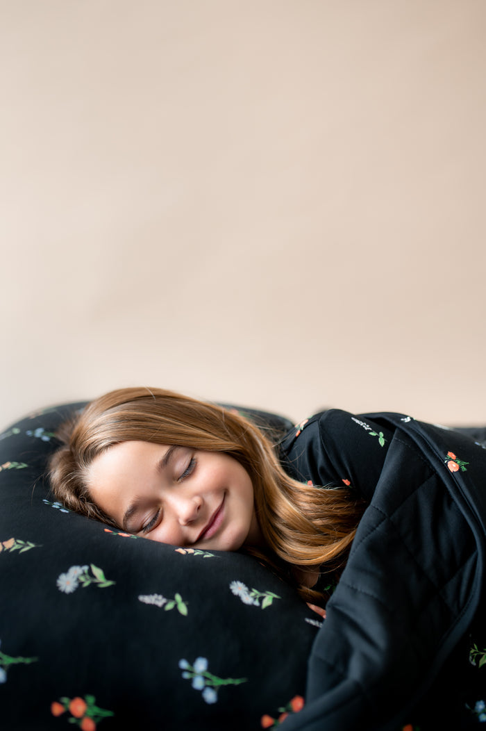 Girl sleeping on Standard Pillowcase in Midnight Wildflower print covered under a similar print youth blanket on a beige background
