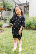 Girl standing outdoors in grass wearing Toddler Biker Short Set in Midnight Wildflower print and pink boots