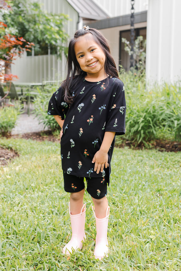 Girl standing outdoors in grass wearing Toddler Biker Short Set in Midnight Wildflower print and pink boots