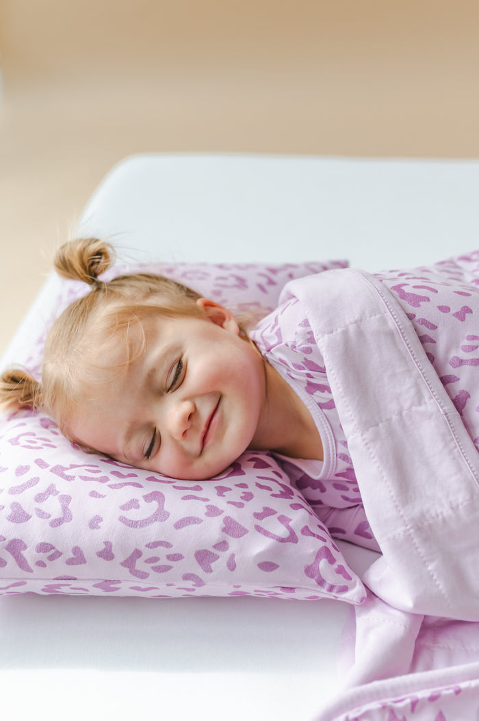 Child lying under a Thistle Leopard print Toddler blanket on a toddler pillowcase and wearing a similar print shirt on a white sheet