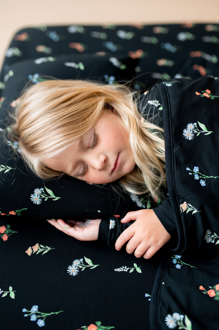 Girl sleeping on Toddler Pillowcase in Midnight Wildflower print covered under similar print Toddler blanket and sheets