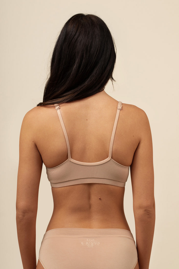 Woman wearing a beige bra and underwear set against a beige background