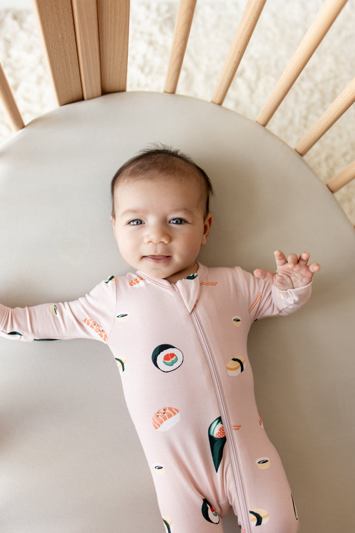Baby lying in crib wearing pink Zippered Footie in Sushi print
